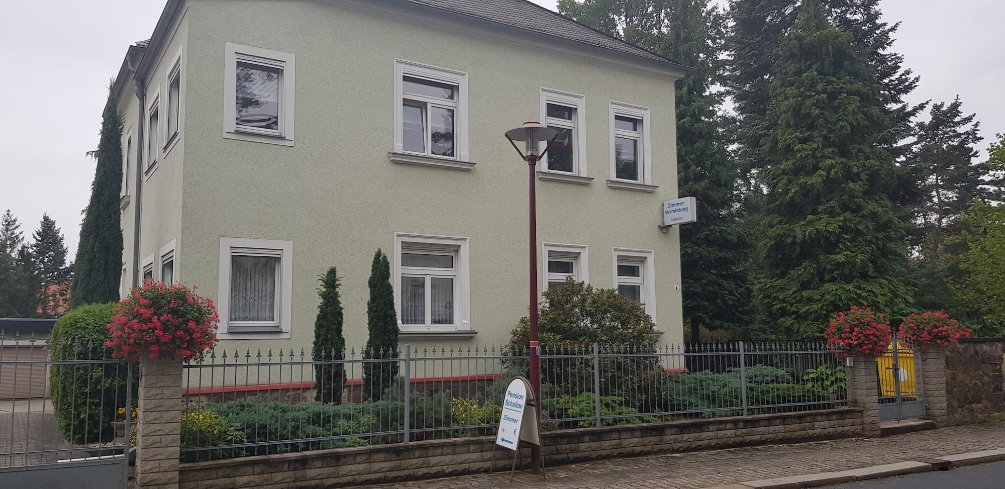 Das hellgrüne Haus der Pension Schallon in der Karl-May-Straße 4 mit dem Schild Zimmer-Vermietung Schallon und Geranien am Gartenzaun