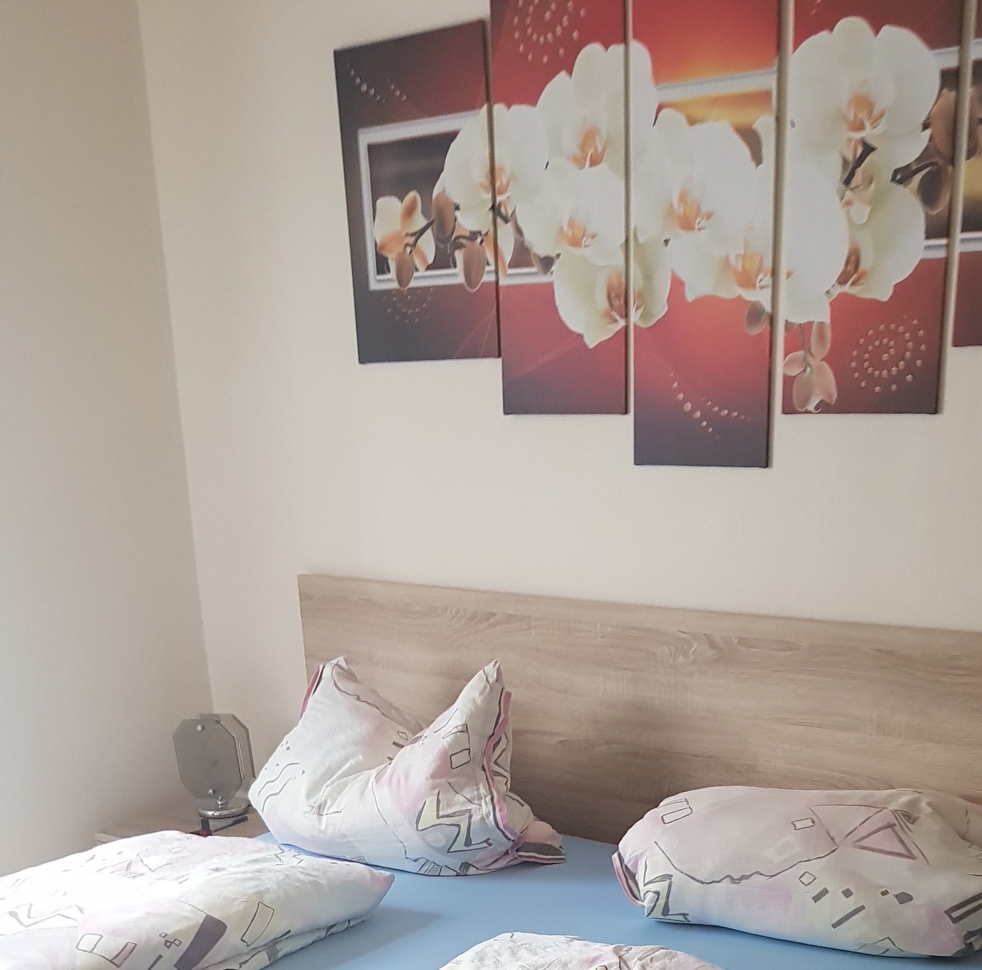Doppelbett mit hellem Holzkopfteil und Orchideen-Wandbild in einem weiteren Gästezimmer